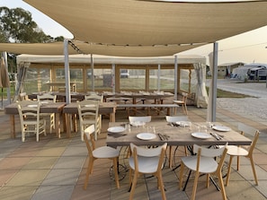 Un área de comedor al aire libre con varias mesas y sillas, cubierta por un amplio toldo.