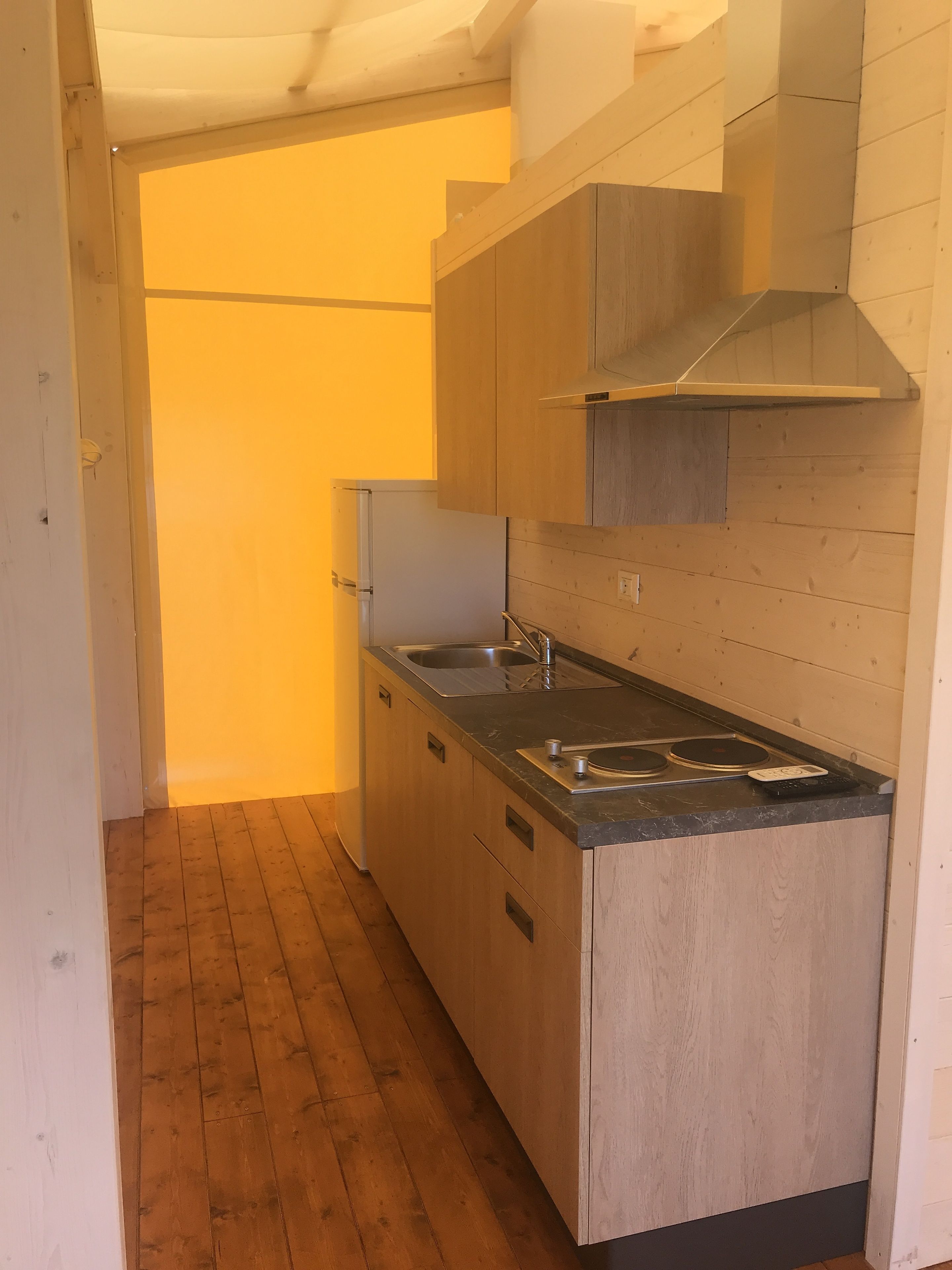 Una cocina compacta con armarios de madera, un lavamanos de acero inoxidable y una estufa empotrada.