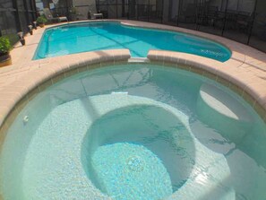 A swimming pool with a circular hot tub in the center, surrounded by a tiled deck.