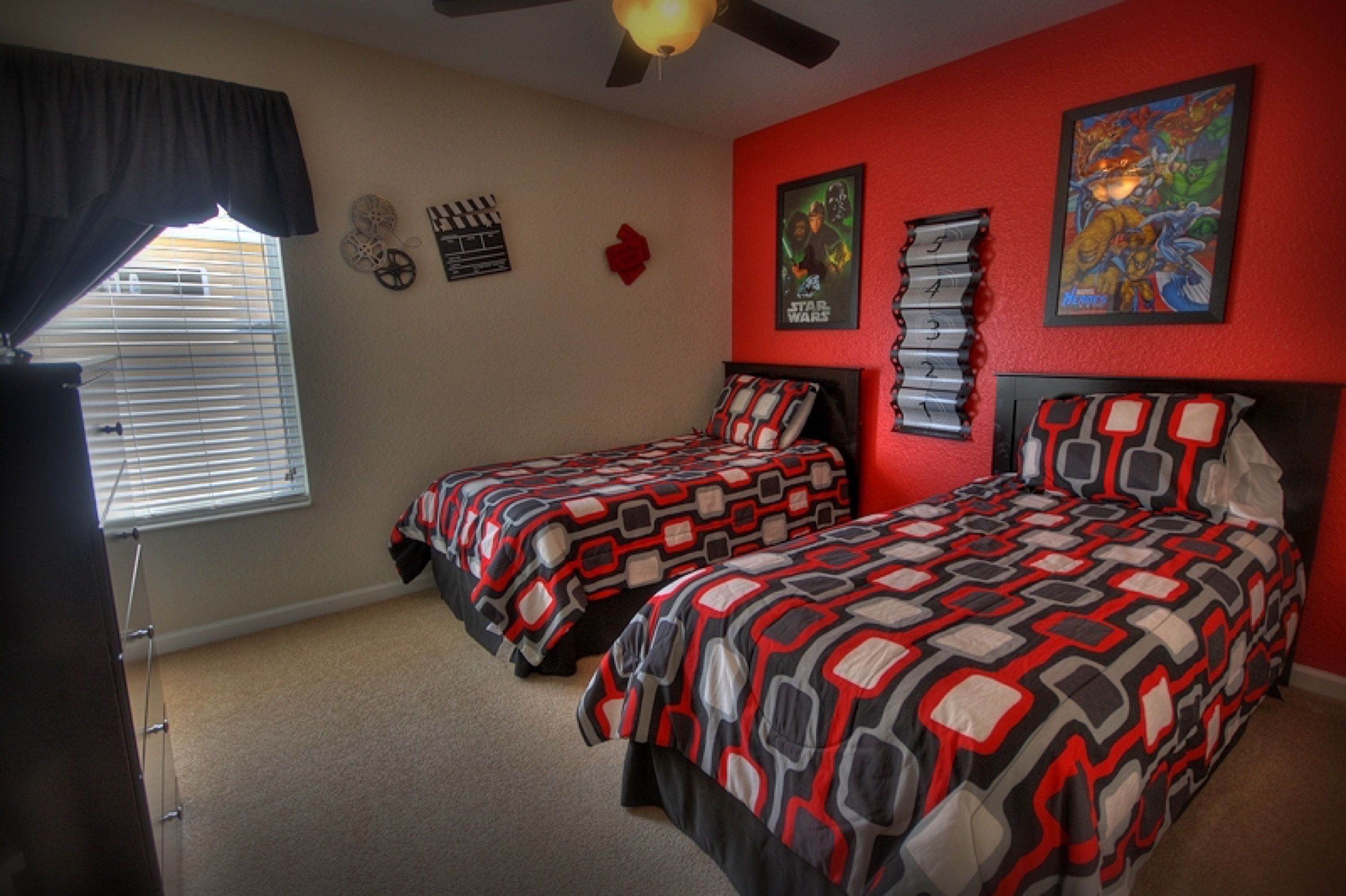 A bedroom with two beds, a ceiling fan, a window with blinds, and wall decorations including posters and a clock.