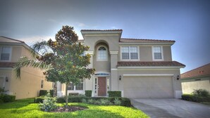 A two-story house with a front garage, a small front yard with a tree, and a well-maintained lawn. - 6BR 4BA Home in Windsor Hills by CV-2579 (Kissimmee)