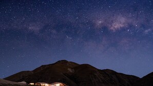A mountain with a lit building at its base, under a starry night sky. - The Lindis (Birchwood)