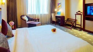 A hotel room with a bed, a desk, a chair, a TV, and a window with curtains. - Chengdu Yijin Hotel (Chengdu)