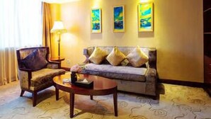 A hotel room with a sofa, armchair, and a coffee table. There are three paintings on the wall and a lamp on the side table. - Chengdu Yijin Hotel (Chengdu)
