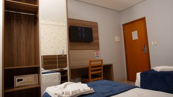 A hotel room with a wooden wardrobe, a desk with a television, a bed with a blue blanket, and a door with a sign.