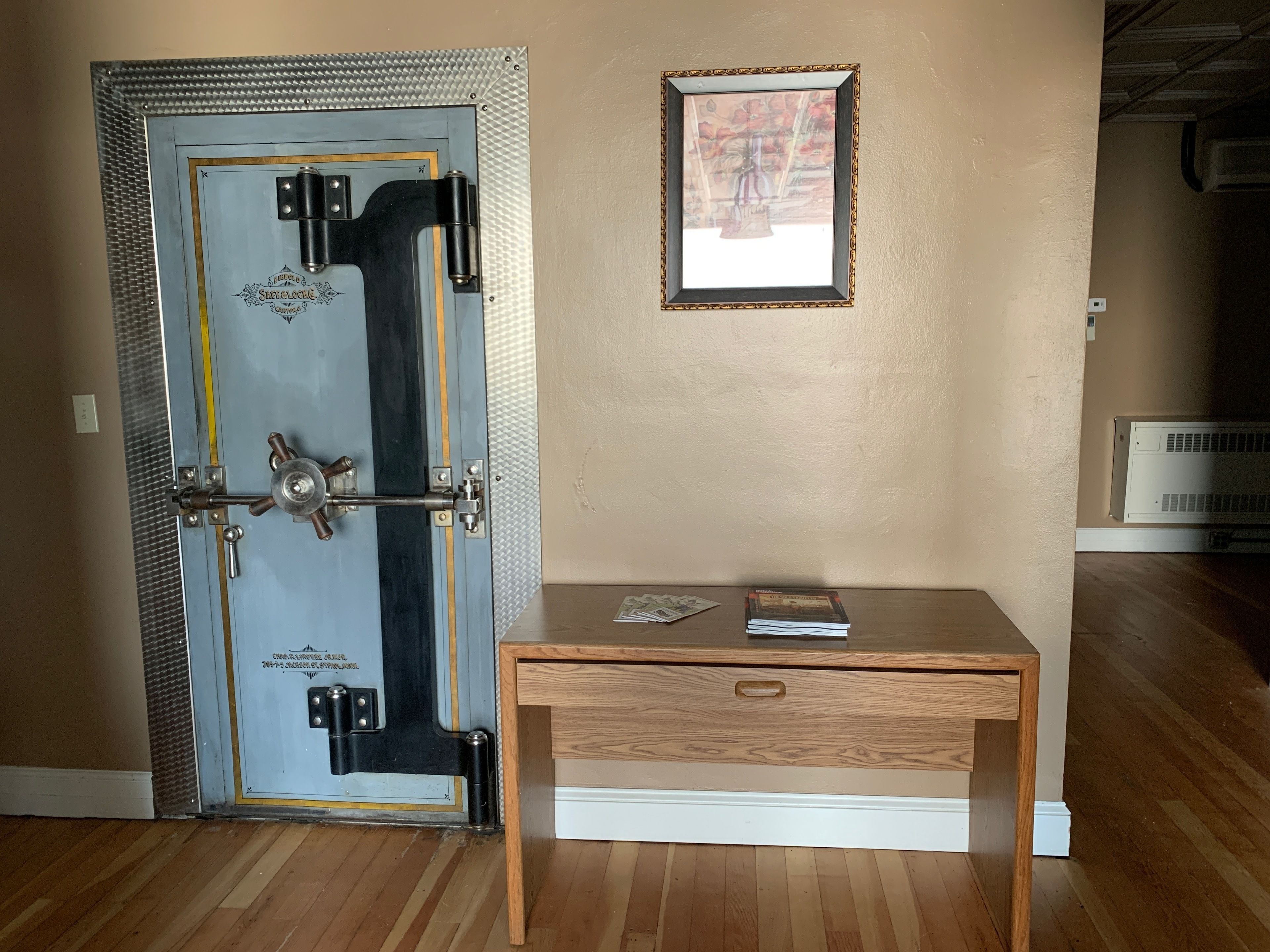 Una habitación con una caja fuerte grande, un escritorio de madera y un cuadro en la pared.