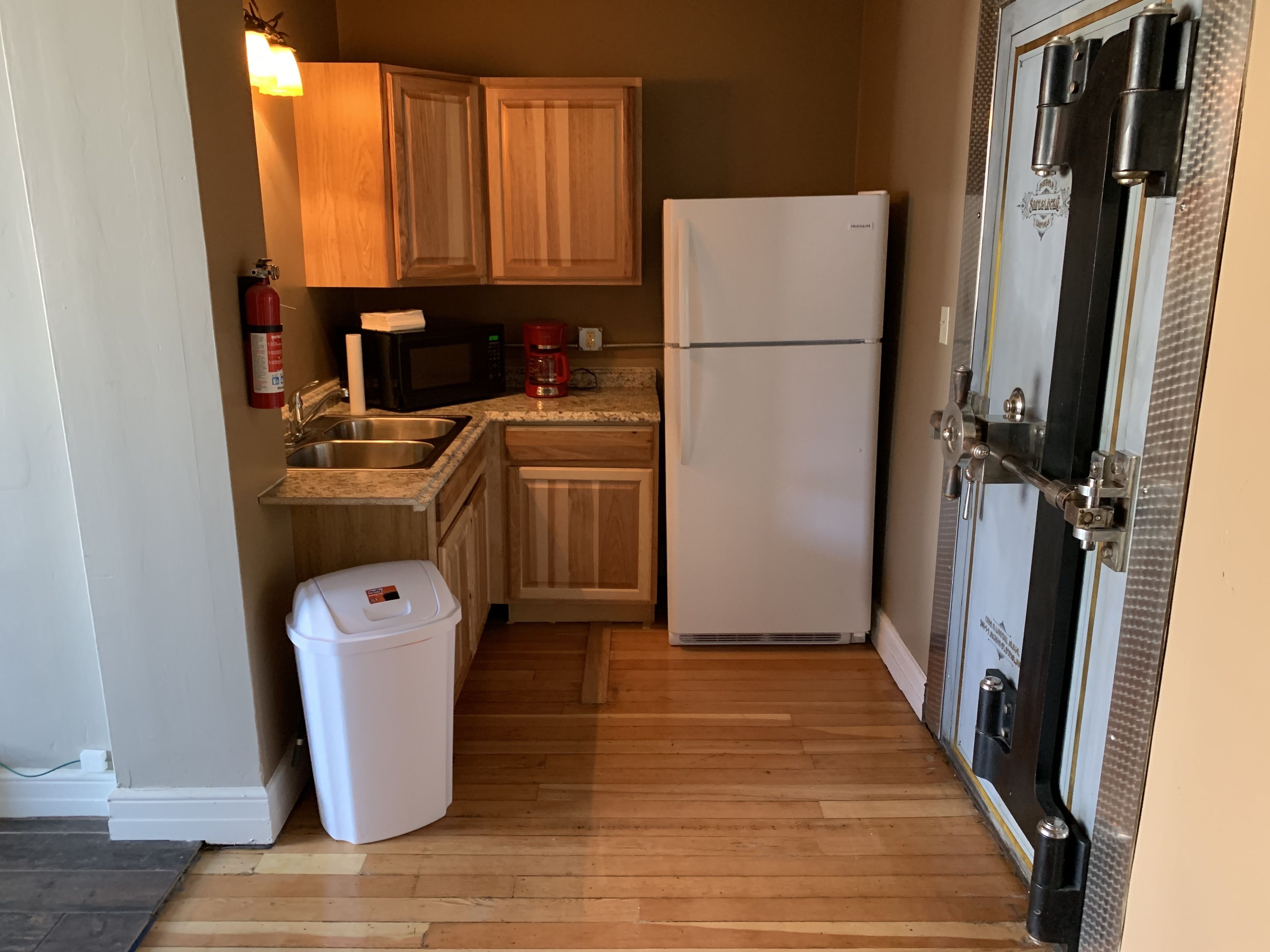 Una cocina compacta con armarios de madera, un refrigerador blanco, un microondas y una cafetera.
