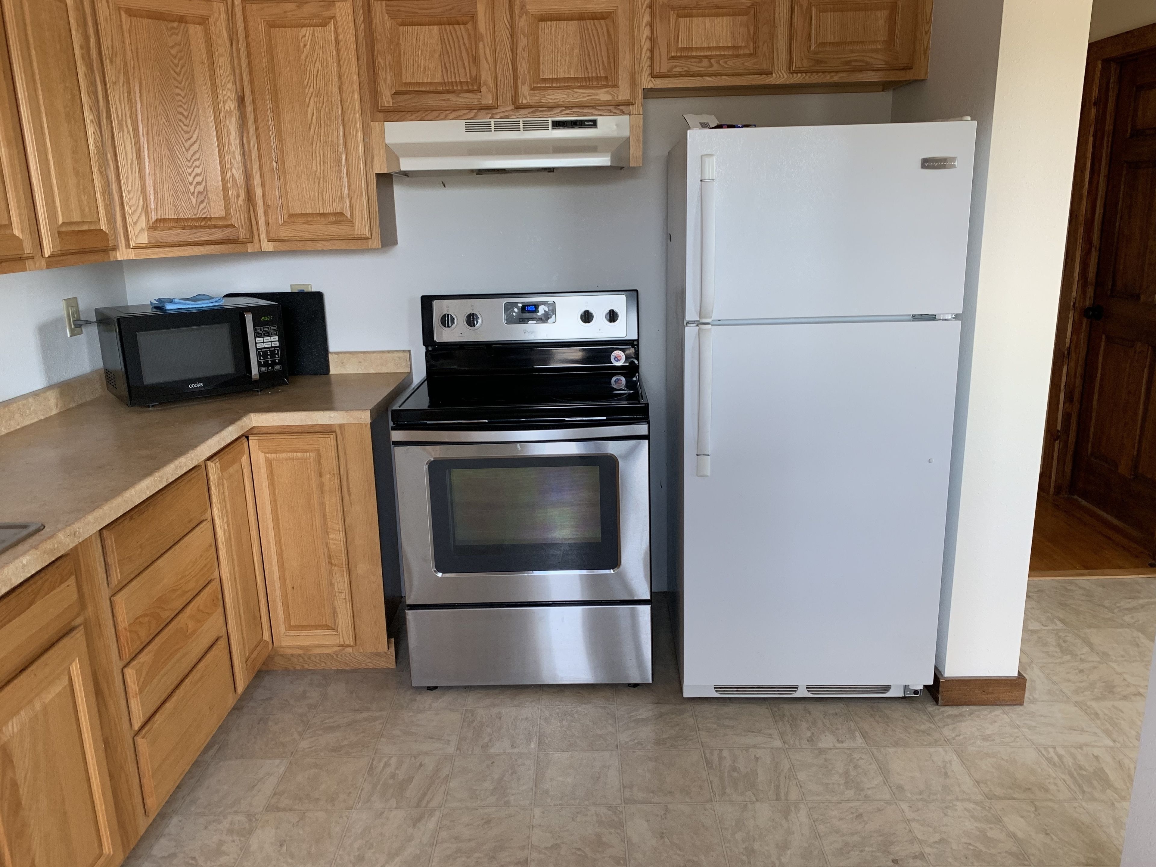 Una cocina con armarios de madera, una estufa de acero inoxidable, un microondas y un refrigerador blanco.