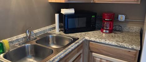 A kitchen with two stainless steel sinks, a black microwave, and a red coffee maker.