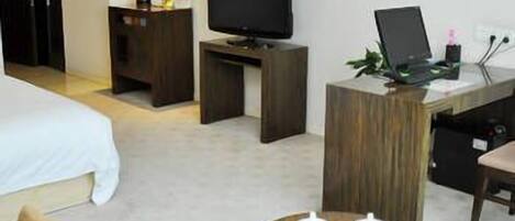 Una habitación de hotel con cama, televisión, escritorio con una computadora portátil, mesa de centro con tazas y sofá.
