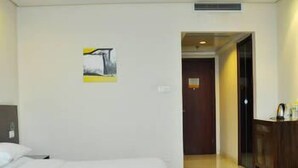 A hotel room with a bed, a wooden dresser, and a door leading to another room. - Lin Yi Hotel (Linyi)