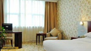A hotel room with a large bed, a desk with a computer, a chair, a small table, and a lamp. - Lin Yi Hotel (Linyi)