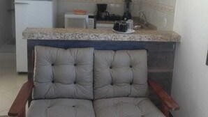 Une cuisine compacte équipée d’un réfrigérateur, d’une machine à café et d’un évier. Une chaise rembourrée est placée devant la cuisine.