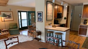 Uma sala de jantar com uma mesa e cadeiras de madeira, uma cozinha com armários de madeira e uma sala de estar com sofá e poltrona.