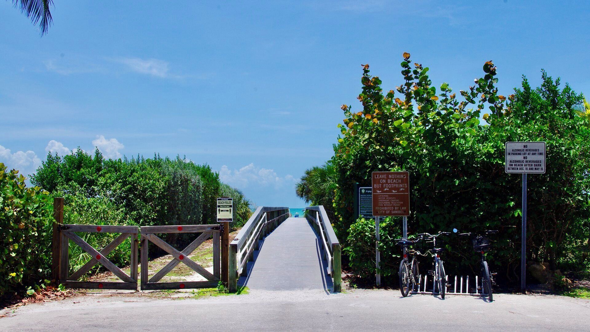 Un pont en bois mène à une plage où un panneau interdit la consommation de boissons alcoolisées et un autre indique qu’il est interdit de se garer à tout moment.