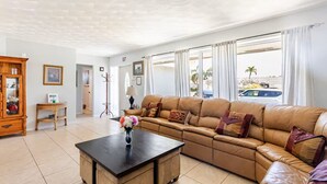 A living room with a leather sofa, a wooden coffee table, a cabinet, and a window with curtains. - Family Retreat w/ Dual Masters - Screened Pool, Media Game Room & Beach 6 Miles (Hollywood)