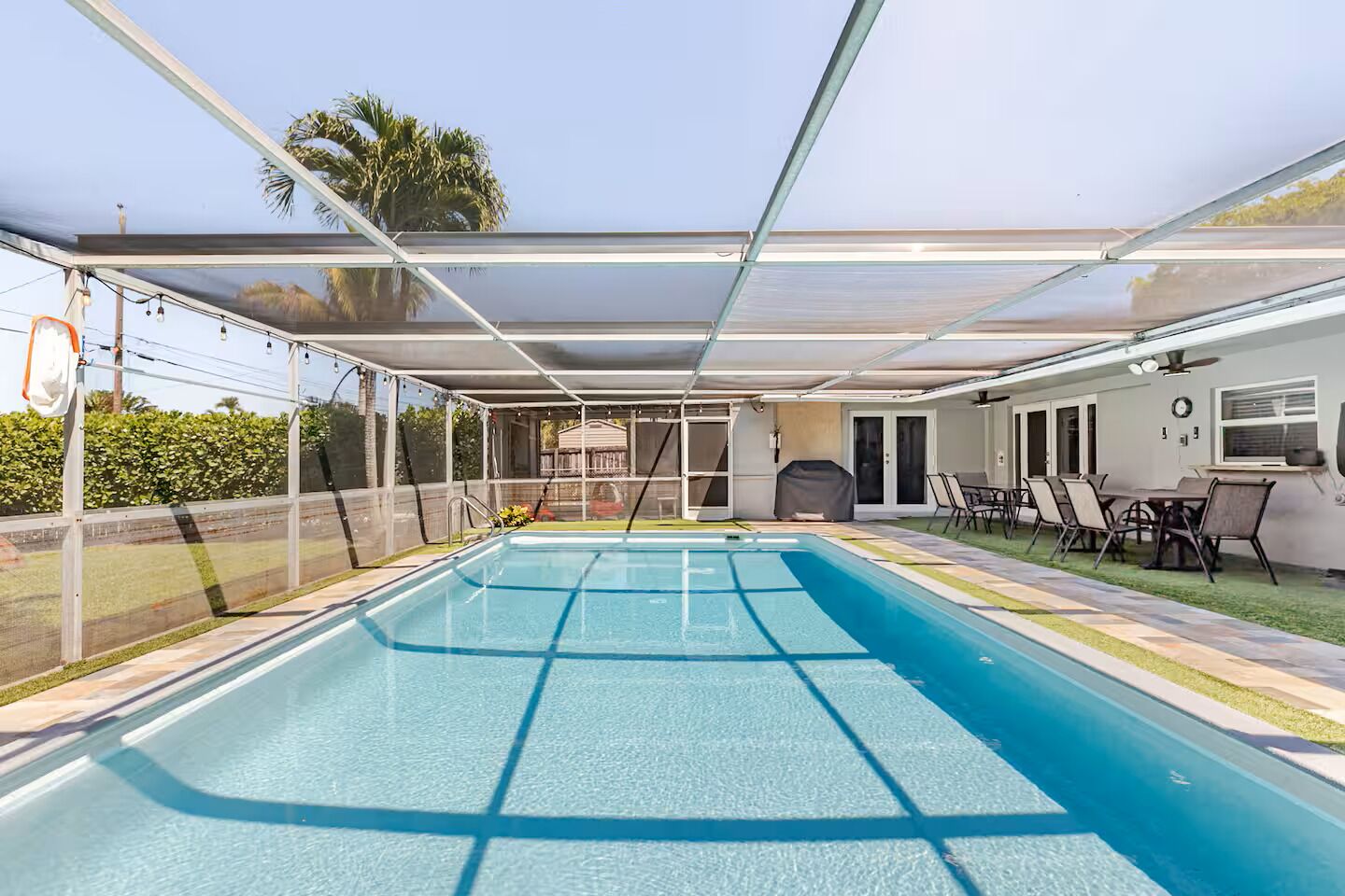 A covered swimming pool with a patio area, outdoor seating, and a view of the house.