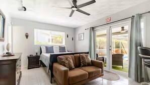 A bedroom with a bed, a brown sofa, a ceiling fan, a window, and an exit sign. - Family Retreat w/ Dual Masters - Screened Pool, Media Game Room & Beach 6 Miles (Hollywood)