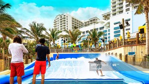 A water slide at a resort with palm trees and a view of a tall building in the background. - Family Retreat w/ Dual Masters - Screened Pool, Media Game Room & Beach 6 Miles (Hollywood)