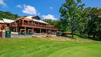 A large, two-story building with a covered porch and multiple windows, surrounded by a well-maintained lawn and trees.