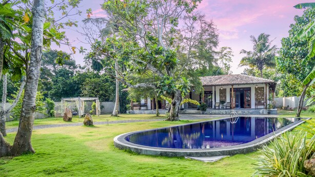 Une piscine entourée d’une végétation luxuriante, un belvédère et une maison avec un toit en tuiles.