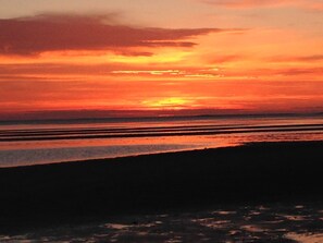 Un coucher de soleil sur une plage, les eaux calmes reflétant le ciel.