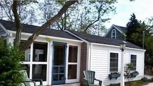 A small white house with a porch, two chairs, and a pathway leading to the entrance. - Steps To Bay at Campground Beach, A/C, Heat,Wifi, Outdoor Shower, Gas Grill (Eastham)