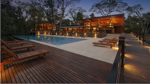 Un resort moderno con piscina, terraza de madera y un edificio con grandes ventanales.
