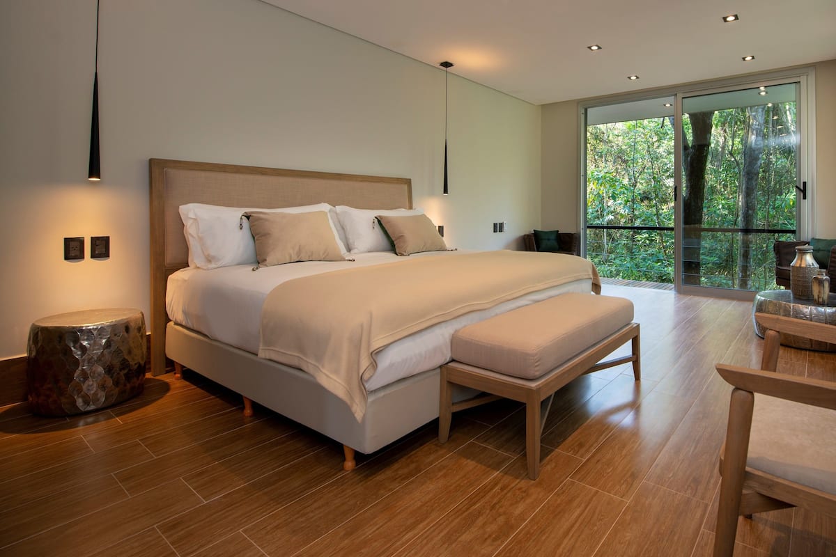 Un dormitorio moderno con una cama grande, un banco de madera, una silla y vistas al exterior.