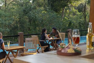 A wooden deck with outdoor seating overlooking a pool and lush greenery.