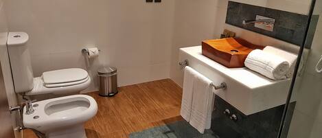 A modern bathroom with a toilet, bidet, and a sink with a wooden basin.