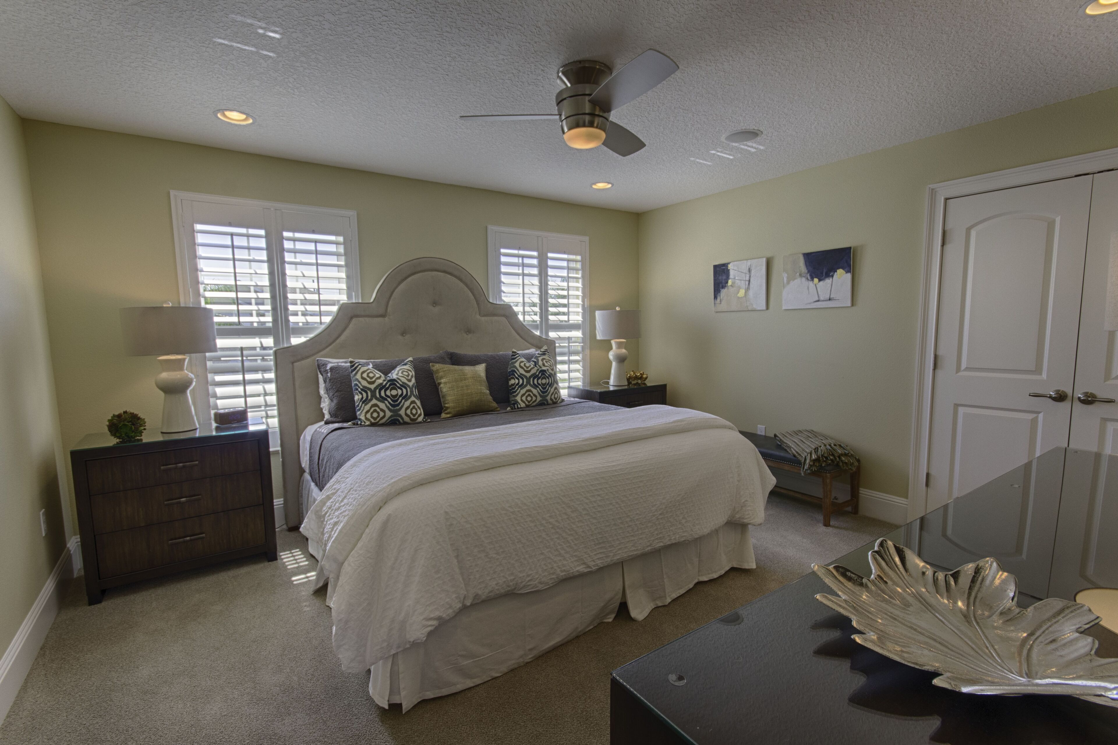 A bedroom with a bed, nightstands, a dresser, a ceiling fan, and a door.