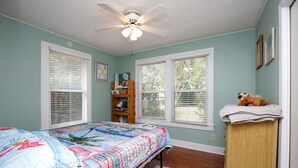 A bedroom with a bed, a ceiling fan, a wooden dresser, and a window with blinds. - Flamingo Pad | Pet-Friendly Pensacola Rental Near Downtown & Pensacola Beach (Pensacola)