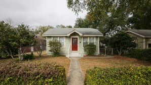 A small, single-story house with a red door and a front yard. - Flamingo Pad | Pet-Friendly Pensacola Rental Near Downtown & Pensacola Beach (Pensacola)