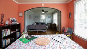 A room with a bed, a bookshelf, a table with a patterned tablecloth, and a window with blinds. - Flamingo Pad | Pet-Friendly Pensacola Rental Near Downtown & Pensacola Beach (Pensacola)