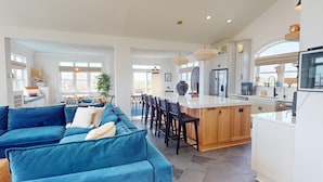 Ein geräumiger Wohnbereich mit blauem Sofa, Esstisch aus Holz und einer Küche mit weißen Schränken und Edelstahlgeräten.
