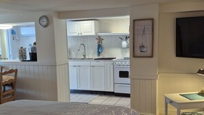 A bedroom with a bed, a small table with a lamp, and a view into a kitchen with white cabinets and a stove. - I'm the ONE! The CONCH Walk to Beach and Times Square (FMB)