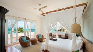 Ein Schlafzimmer mit einem großen Bett, einem Deckenventilator und Blick auf das Meer durch große Fenster.