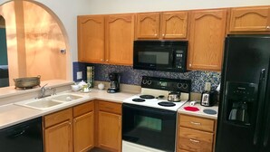 Une cuisine avec des meubles de rangement en bois, un micro-ondes noir, une cuisinière, un évier et un réfrigérateur.