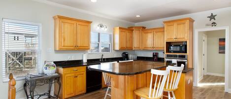 A modern kitchen with wooden cabinets, a large island with bar stools, and a built-in microwave.
