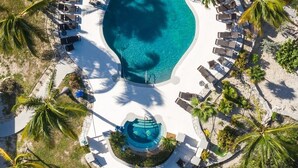 Vue aérienne d’un complexe hôtelier doté d’une grande piscine, de chaises longues, de palmiers et d’un petit toboggan aquatique.