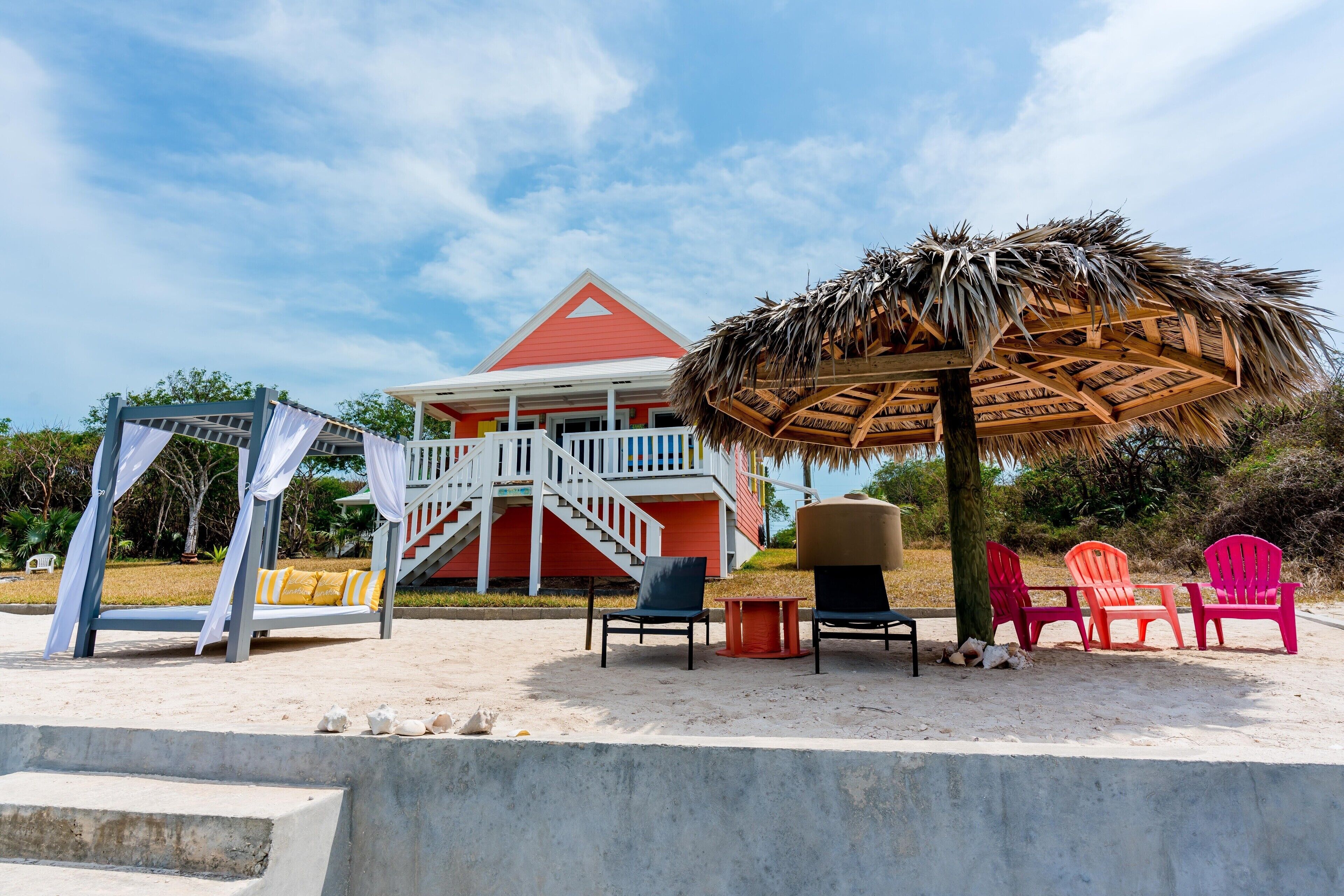 A beachside resort with a red building, a thatched umbrella, and beach chairs.