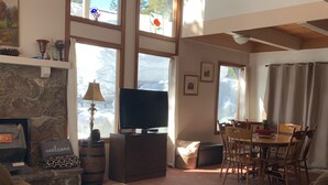 A cozy living room with a stone fireplace, a television, and a dining area with wooden furniture.