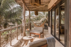 A balcony with a hammock, a cushioned chair, and a small round table with a vase. - 4BR Beachfront Villa Ideal for Groups & Getaways (tulum)
