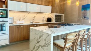 A modern kitchen with a marble countertop, wooden cabinets, and pendant lighting.