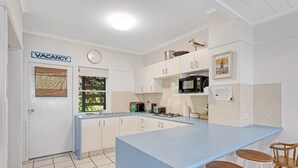 Una cocina con encimera azul, armarios blancos, microondas y un lavabo. Hay un cartel de 'VACANCY' en la puerta.