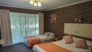 A hotel room with two beds, a brick wall, a large window with curtains, and a ceiling light fixture. - Barham Colonial Motel (Barham)