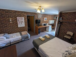A room with two single beds, a desk with a computer and a microwave, a small refrigerator, and a television.
