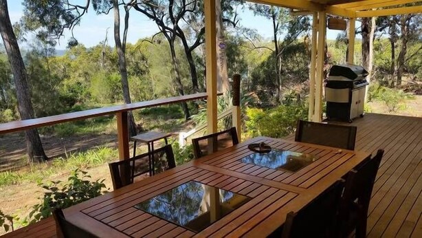 Una terrassa de fusta amb taula i cadires, amb vista a un paisatge natural ple d'arbres i una visió de l'horitzó.