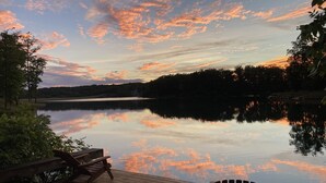 Une terrasse en bois avec une chaise et un banc, donnant sur un lac paisible et un ciel au coucher du soleil.